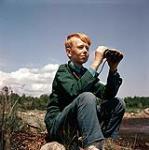 Macoun Club, Ottawa - boy sitting next to the Rideau River with binoculars. March 22, 1963
