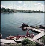 High shot of dock at Stony Lake. Two boats, with people preparing for motor boat ride.  août 1951.