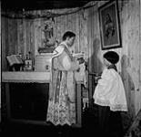 Prêtre et un enfant de choeur célébrant la messe devant une image de Jésus dans une structure en bois   n.d.