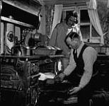 Sandy Lunan, agent de la Compagnie de la Baie d'Hudson, cuit du pain et un autre homme l'observe, Baker Lake, T.N.O. [Baker Lake (Qamanittuaq), Nunavut]. mars 1946.