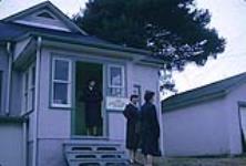 Three women in uniform standing outside building. November 1961