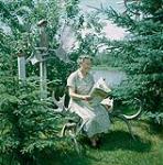 Woman reading on a bench made of moose antlers, Manitoba  June, 1956.