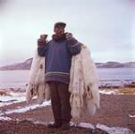 Man carrying fox pelts, Cape Dorset, Nunavut.  [between June-September 1960].