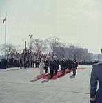 [La reine Élizabeth et le prince Philip debout devant le Mémorial national de la guerre, dimanche matin le 13 octobre 1957, rendant hommage aux Canadiens morts durant le conflit alors que l'on entend l'hymne national et le son des clairons. Le couple royal est accompagné: de gauche à droite: le ministre des Anciens Combattants, l'honorable A.J. Brooks, Mme J.Diefenbaker, l'honorable John G. Diefenbaker, le Premier Ministre, l'honorable G.R. Pearkes, le ministre de la Défense nationale, président de la légion canadienne et des réprésentants de groupes d'anciens combattants.] 13 octobre 1957.