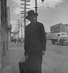 Winnipeg, années 1940. Homme non identifié sur le trottoir avec une valise [entre 1940-1949]