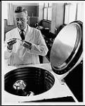 Dr. Edward O. Dodson, professor of biology and world renowned expert on genetics, studies the mutagenic effects of centrifugal force on an expensive refrigerated centrifuge. University of Ottawa (?). Department of Citizenship and Immigration, Information Division [between 1930-1960]