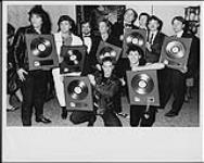 Les membres du groupe Honeymoon Suite acceptent une palme d'or pour leur premier disque, « Honeymoon Suite », après le gala des prix Juno : (debout) Dave Betts, Johnny Dee, Garry Newman (VP commercial, WEA), Ray Coburn, Stan Kulin (président, WEA), Bob Roper (directeur, A&R, WEA), Tom Treumuth (producteur du groupe), Steve Prendergast (impresario du groupe), (à genoux) Derry Grehan, Gary Lalonde. [ca 1985].