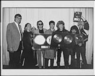 Le groupe Hall and Oates reçoit un album double platine pour « Big Bam Boom » après un spectacle à Toronto : (de gauche à droite) Don Kollar (directeur général, RCA), G.E. Smith (guitariste), Randy Hoffman (vice-président, Champion Entertainment), Charlie Dechant (saxophoniste), Mickey Curry (batteur), Daryl Hall, John Oates, T. Bone Wolk  [entre 1984-1985].