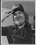 B. W. Pawley wearing a baseball cap, standing beside a microphone  [between 1982-1985].