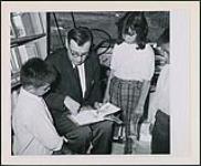 Daniel D. Sudar, bibliothécaire en chef de la Northwestern Ontario Regional Library faisant la lecture à trois enfants : Don Fairfield, Russ Fairfield (droite) et Alice Barnard, dans un bibliobus n.d.