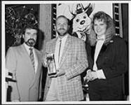 Cliff Dumas de CHAM reçoit le prix de la « personnalité radio de l'année » remis par Carmen Westfall et Leonard Rambeau, de Balmur Ltd. [entre 1990-1992].