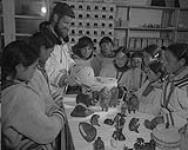 James A. Houston, of the Canadian Handicrafts Guild, shows a group of Inuit children some baskets made in Cape Dorset   July 1951