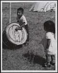 A small boy tries out one of the drums that will be used to beat out a rhythmic accompaniment for the traditional Grass Dance which forms an important part of the ceremonies. 21 August 1959