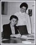 Recording secretary in the new band administrative set-up will be Mrs. Shirley Williams, seated, who receives a word of helpful advice from Mrs. Ruth Anne Nantais. [between 1959-1960]