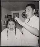 [Ronney Bull Shields, 5, is given his first haircut by Ernie Rabbit, the first First Nations businessman on the Blood Indian Reserve at Cardston, Alberta]. Original title: Ronney Bull Shields, 5, is given his first haircut by Ernie Rabbit, the first Indian businessman on the Blood Indian Reserve at Cardston, Alberta. 1962