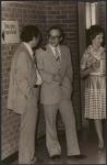 [Two men in conversation beside a woman at a celebration event]. 1975