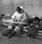 Salomonie at work on model kayak for the Canadian Handicrafts Guild.  Daughter Annie keeps him company. Cape Dorset (Kinngait), Nunavut.  n.d.