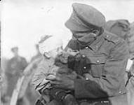 A Canadian Artilleryman tries to amuse a little Belgian baby, whose Mother was killed by a German shell. November, 1918 November, 1918.