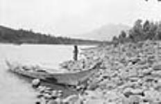 A Gitxsan First Nation girl fishing in the Skeena River at Kitwanga (Gitwangak/Gitwangax), British Columbia, with a dugout cedar canoe in the foreground and two more in the background 1915.