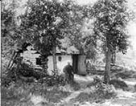 [Man sitting outside log cabin in woods.] 1868-1923