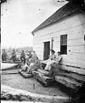 Men and women outside a log cabin n.d.