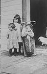 Two young girls standing on a wooden porch beside a boy in a cradle board, Temagami First Nation, probably Lake Temagami, Ontario n.d.