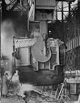 Close-up of teeming molten steel from a 180-ton ladle into ingot moulds. The Steel Co. of Canada Ltd., Hamilton, Ontario