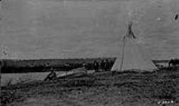 First Nations men outside of a tipi (tepee/teepee) and another man sitting beside a canoe at their camp in Alberta 1922