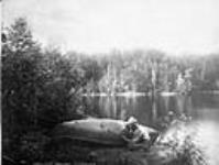 Gumming a leak in bark canoe at Bullfrog Camp c.a. 1887
