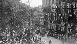 Parade passing flag-decorated buildings during celebration of an unidentified event ca. 1900-1914