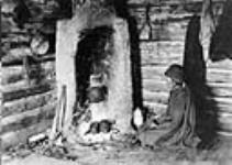 Native Indian woman beside rustic fireplace in log dwelling 1911