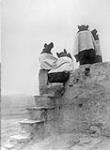 A group of [Hopi] girls on the topmost roof of Walpi, [Arizona] watching the dancers down in the plaza 1922