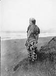 A Tolowa woman in the gala costume of the Coastal Athabascans; [north west California]. The dress is a deerskin kilt with the opening at the front protected by a fringed apron of deerskin or of bark 1924