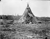 First Nations woman and children sitting at the entrance of a tipi (tepee/teepee), Fort Chipewyan, Alberta 1893