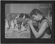 Jeune artiste appliquant la couleur sur les petites sculptures à l'atelier de Monsieur André Bourgault, sculpteur de renommée internationale n.d.