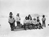 Group of Inuit standing and sitting around a komatik 1928.
