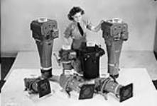 Unidentified airwoman displaying types of aerial cameras used by the Royal Canadian Air Force in Operation Eclipse to photograph a solar eclipse. R.C.A.F. Station Rockcliffe, Ontario, Canada, 19 July 1945 19-Jul-45