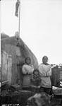 Autochones, chien et « topek », Pond Inlet, côté nord-est, Île de Baffin, T.N.-O. [De gauche à droite : Niigug Inuujaq, Arnaujaq et Moses Ittukusuk photographiés près de l'entrepôt de farine de la Compagnie de la Baie d'Hudson.] 17 Septembre [1924]