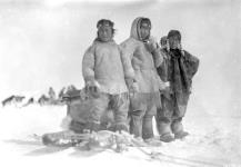 Photograph of two Inuit men and one Inuit woman standing in the snow in front of a komatik (sled) at Qamani'tuaq, Nunavut 1926.