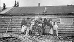 George Weetaltuk and his family in front of a log cabin [Back row: Adla (far left), married to William, George's oldest son (2nd from left), George (centre) and his first wife, Ugugak (4th from left). Front row: George's sons Alaku (far left) and Tommy (sitting on the ground).] 1927.