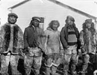 Group of natives at Police Post, Pond Inlet, N.W.T., ca 1923. [Left to right: Siniqaq, Iqipiriaq, Akumalik, Nutaraarjuk and Javagiaq. They were among those attending the trial for the murder of Robert Janes. The R.C.M.P Detachment is in the background.] 1923
