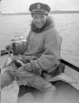 Inuk boy at outboard motor, Cambridge Bay, N.W.T., [Johnny Tologanak. He served as a special constable with the R.C.M.P. during the early 1950s.] [c.a. 1947]