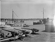 Group of 6in. guns awaiting installation in "H.M.C.S. Prince David". Ship at right is a 'Basset-class trawler of the R.C.N., and ship in centre background is "M.V. M.F. Therese." 19 Aug. 1940