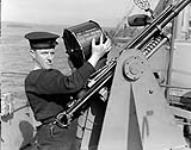 Unidentified naval rating loading an ammunition drum onto a Hispano 20mm anti-aircraft gun aboard an unidentified ship, Halifax, Nova Scotia, Canada, May 1941 May 1941.