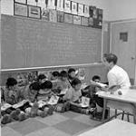 [Miss Velma MacDonald teaching English to First Nation and Inuit children, Inuvik, Northwest Territories, Dec. 1959] Original title: Miss Velma MacDonald teaching English to Indian and Eskimo [First Nation and Inuit] children, Inuvik, N.W.T., Dec. 1959 Dec. 1959.