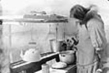 [Annie Kadlutikafaaluk boiling water and baking bannock on "kudlie" (seal-oil lamp).] 1949-1950