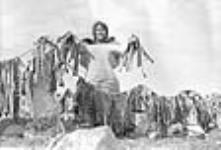 [Femme inuk, Aggiaq, prés d'un séchoir à poissons, Taloyoak] Une femme inuite avec du poisson seché, Taloyoak (anciennement Spence Bay), Nunavut 1951.