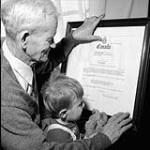 « Le sénateur James Gladstone, de la réserve des Indiens du Sang, montre son certificat de nomination officielle à son petit-fils Jeffrey, âgé de deux ans. » Sept. 1958