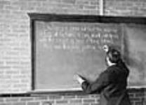 [Lecturer (possibly Nevil Norton Evans) writing on blackboard of laboratory in the W.C. Macdonald Physics Building, McGill University]/Conférencier (peut-être Nevil Norton Evans) écrivant au tableau dans une salle du pavillon de physique W.C. Macdonald, ca. 1895-1900