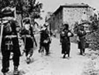 Des soldats canadiens entrent dans un village dont les hommes ont été massacrés par des soldats allemands la semaine précédente 16 jui1. 1944